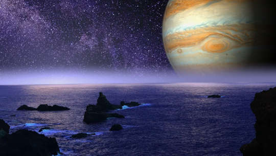 Is Jupiter a Planet of Faith, and Hope or a Planet of Discontent? image of the planet Jupiter on the skyline of a rocky ocean shore