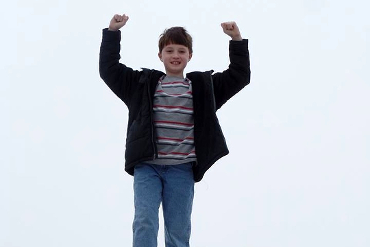 Uplift Yourself, and Others, with Gratitudes a young boy standing with his arms raised in victory