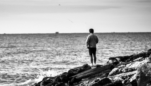 You’re Not Just Watching the Universe — You’re Affecting It Image of a man standing on some rocks looking over at the water. Image by Davide Dalese from Pixabay.